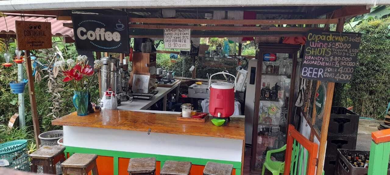 A coffee stand with a wooden counter, a coffee sign, and a menu board listing prices for coffee, shots, brandy, and beer.