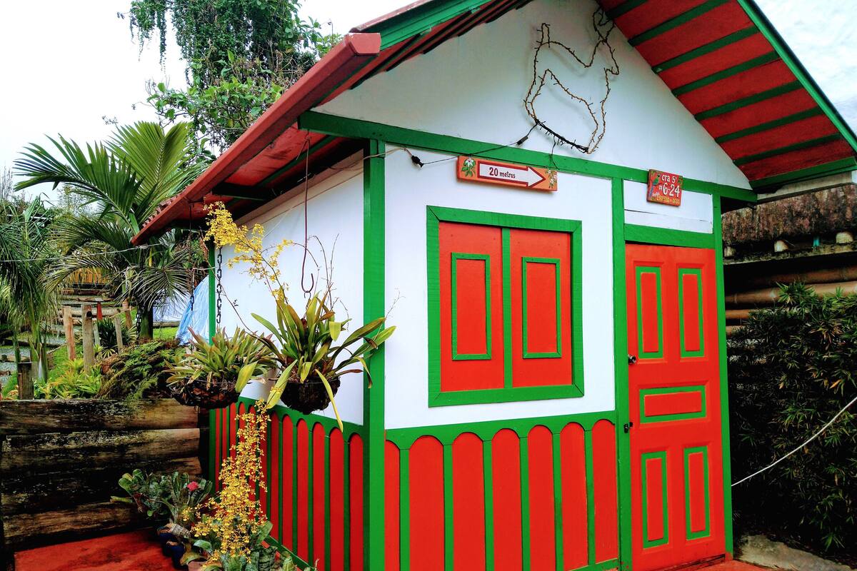 Une petite maison aux couleurs vives, avec une façade rouge et verte, un mur blanc et un panneau indiquant une distance de 20 mètres.