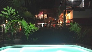 Una piscina por la noche con palmeras circundantes y un edificio al fondo.