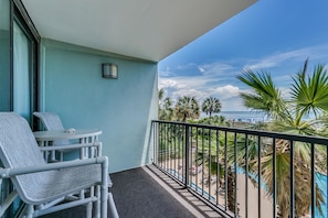 A balcony with a view of a beach, a small table, and two chairs.