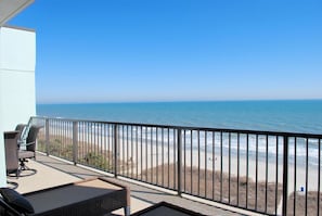 Een balkon met rieten meubilair met uitzicht op een strand.