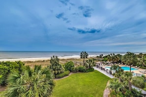 A resort with a pool, beach view, and lush greenery.