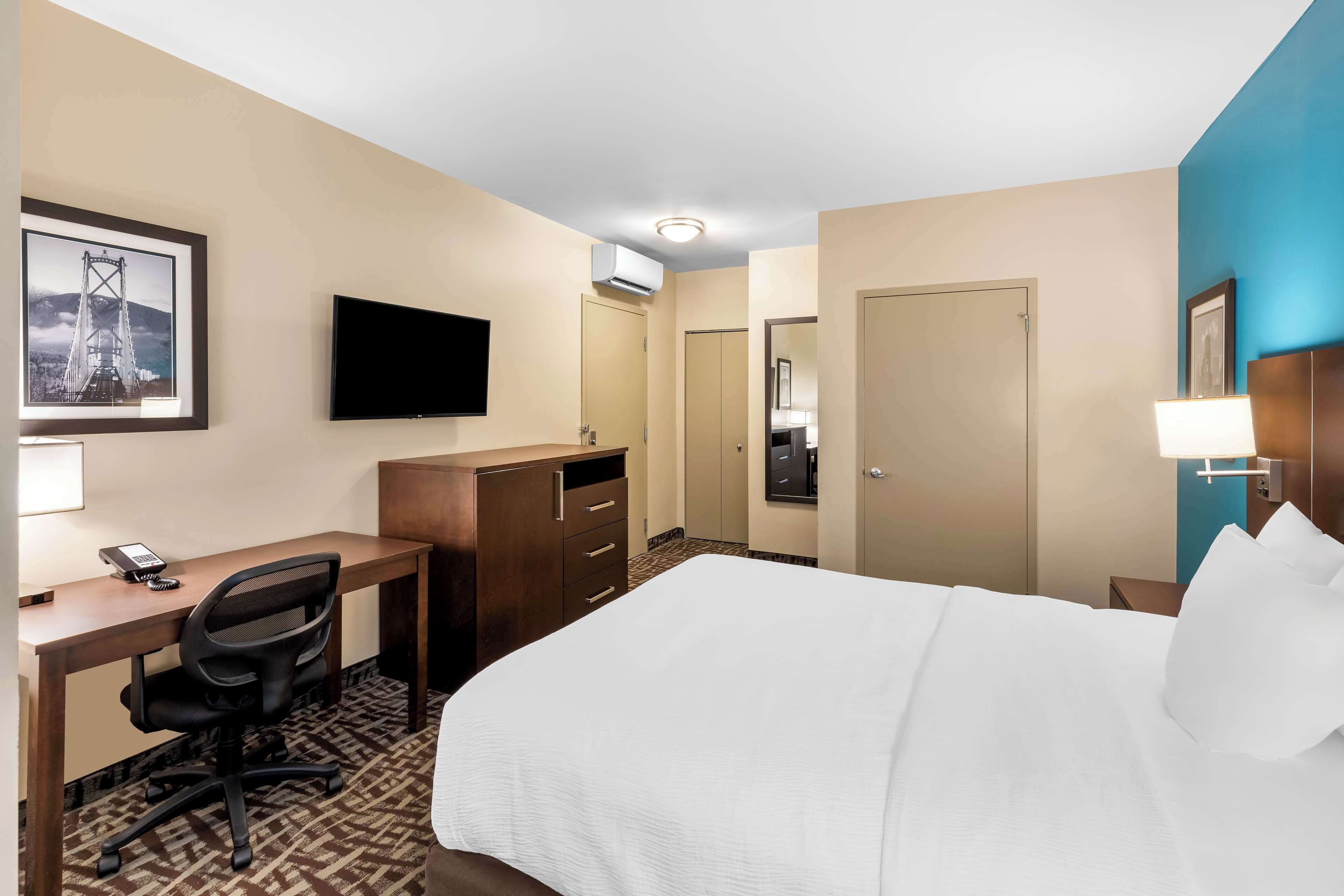 A hotel room with a bed, desk, chair, TV, wardrobe, and a framed picture on the wall.