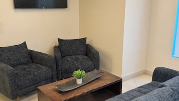 Una sala de estar con dos sofás grises, una mesa de centro de madera y un televisor de pantalla plana montado en la pared.
