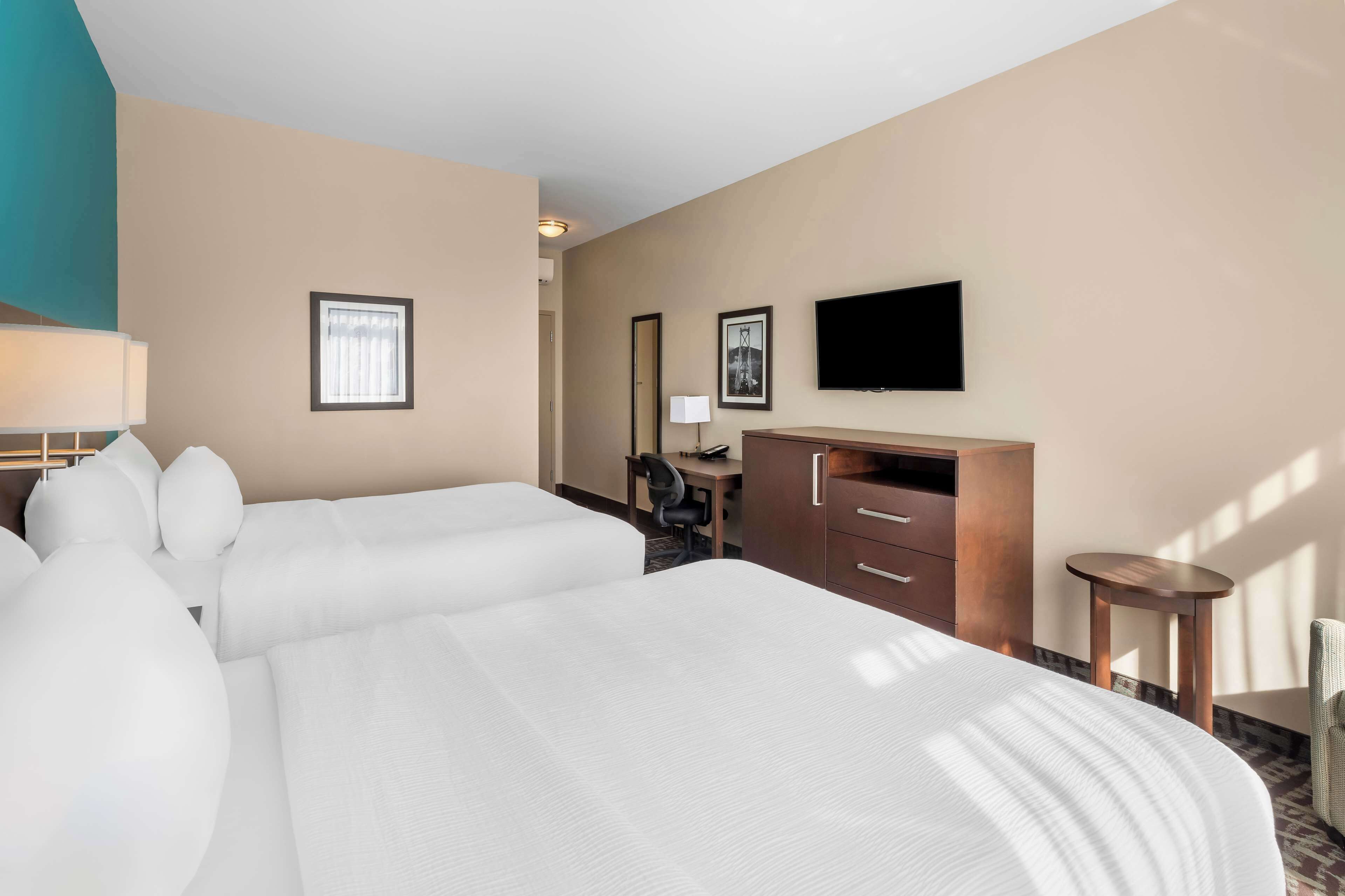 Quarto de hotel com duas camas, uma mesa, uma cadeira, uma televisão e uma pequena mesa.