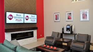 A modern hotel lobby with a fireplace, two armchairs, a sofa, and a flat-screen TV displaying 'Best Western PLUS' signs.