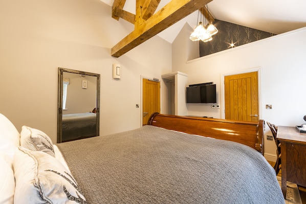 Un dormitorio con cama, cabecero de madera, televisor montado en la pared y una puerta.
