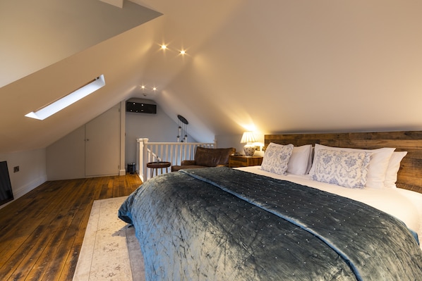 A bedroom with a sloped ceiling, a large bed with patterned pillows, a wooden headboard, and a nightstand with a lamp. - Eagle Mill (Huntingdon)