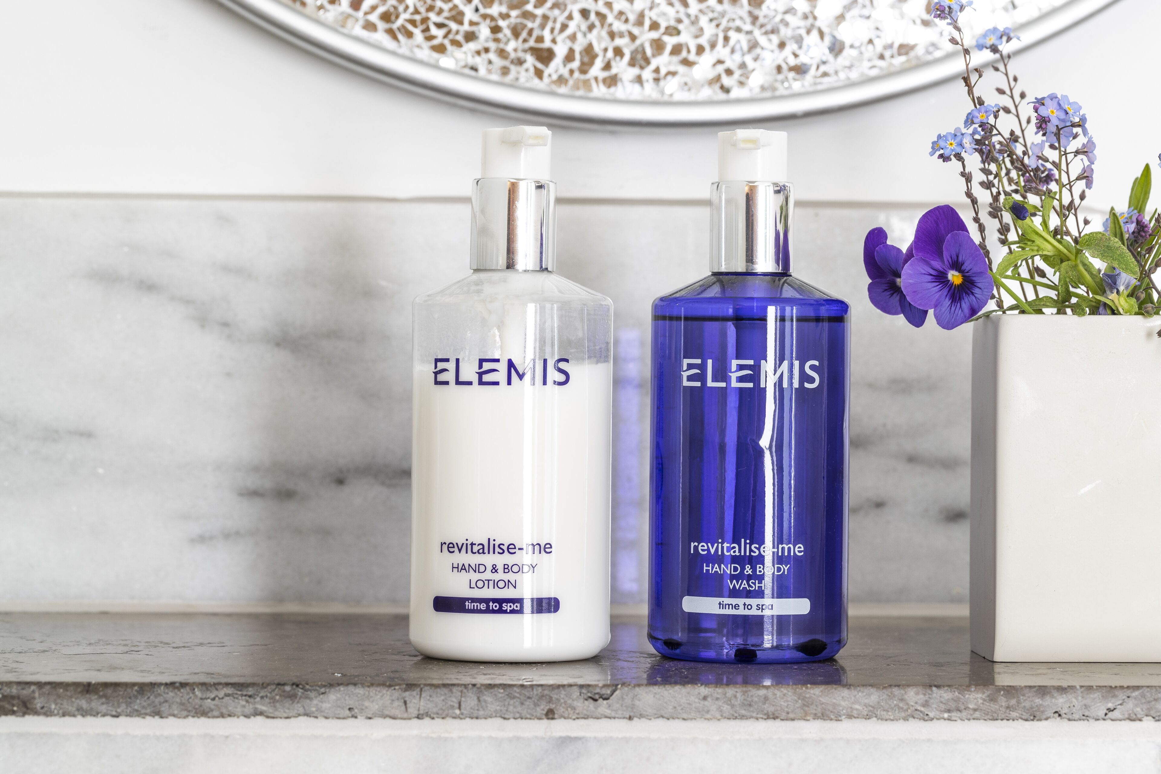 Dos botellas de crema corporal y de manos Elemis sobre una encimera de mármol.