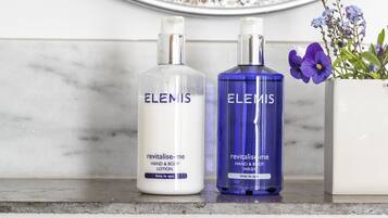 Dos botellas de crema corporal y de manos Elemis sobre una encimera de mármol.