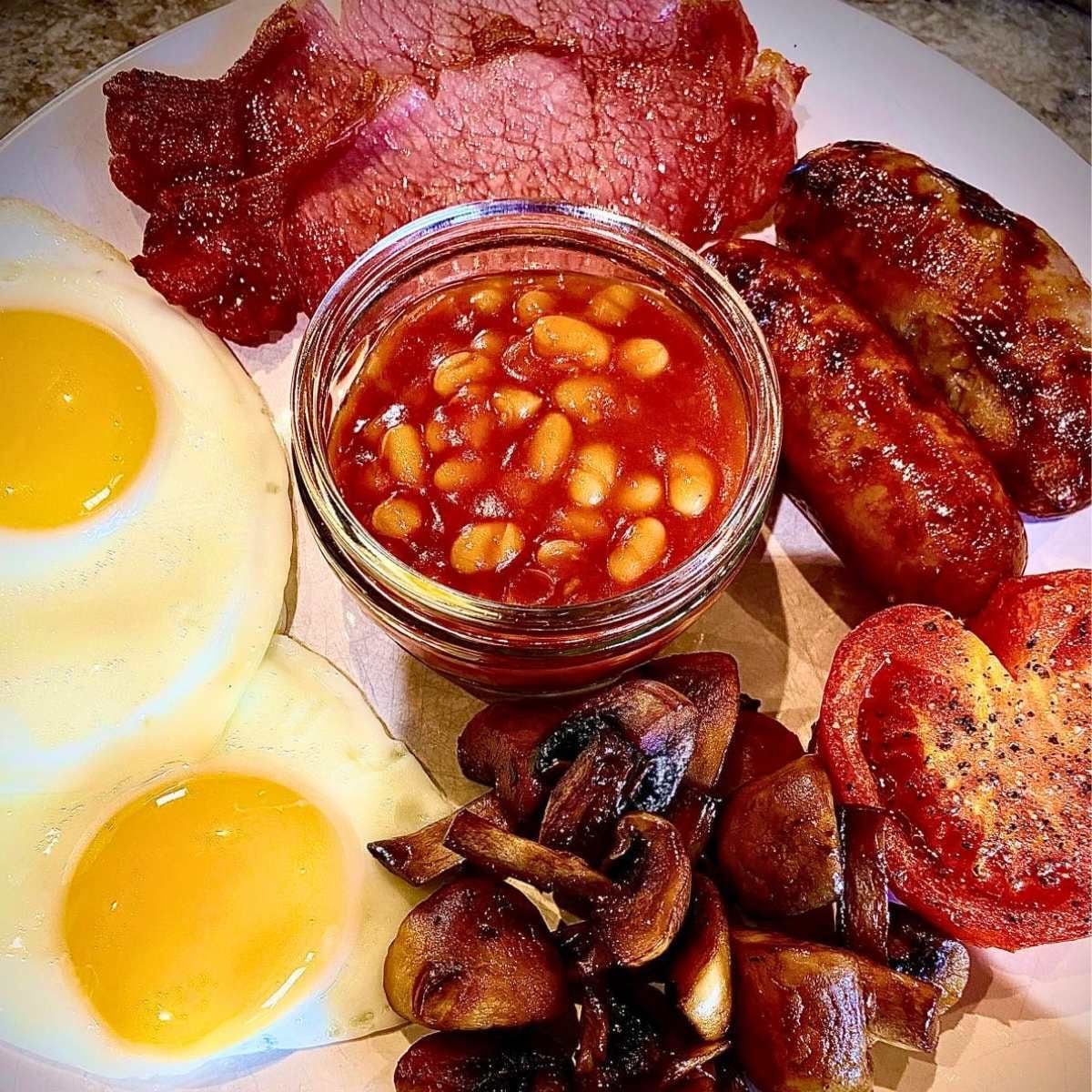 Un plato con huevos, frijoles, tocino, salchichas, champiñones y tostadas.