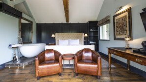 Un dormitorio con una cama grande, una bañera, dos sillones de cuero, un escritorio y una estantería.