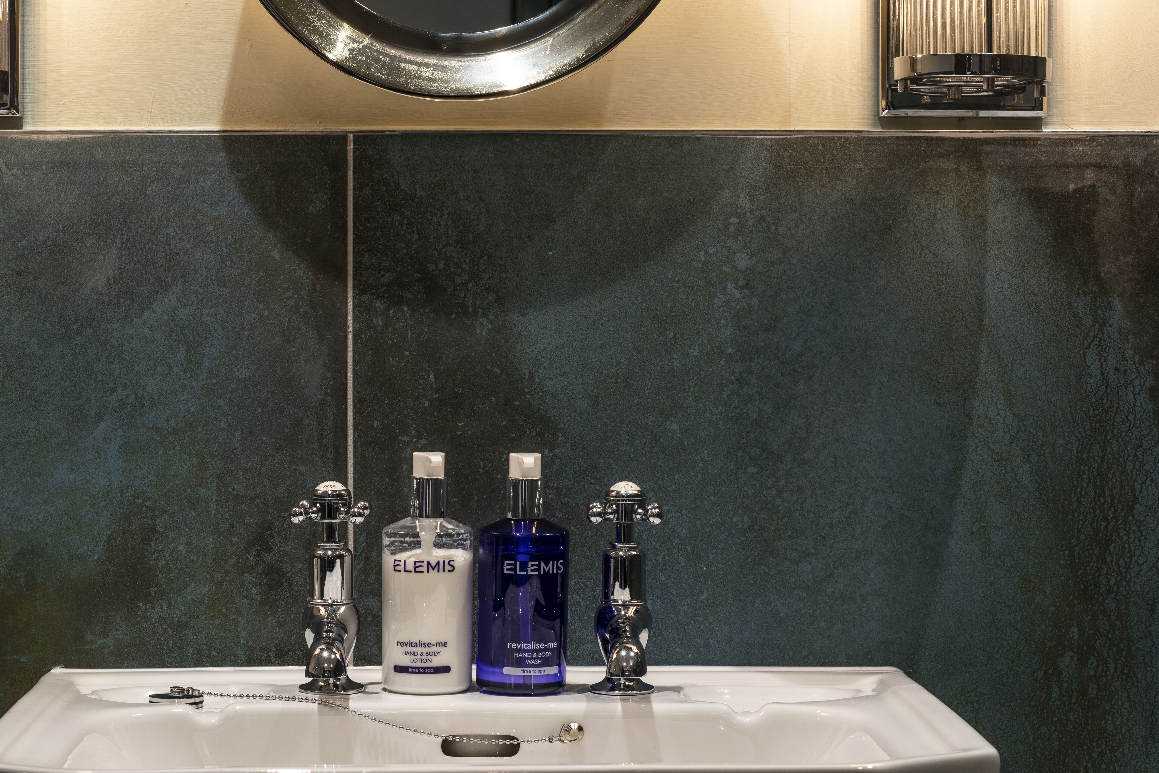 Un bagno con un lavandino bianco, due rubinetti cromati e due flaconi di crema corpo Elemis.
