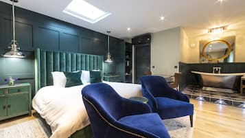 Ein modernes Schlafzimmer mit einem großen Bett, zwei blauen Sesseln, einem Schminktisch mit Spiegel und einer Badewanne.