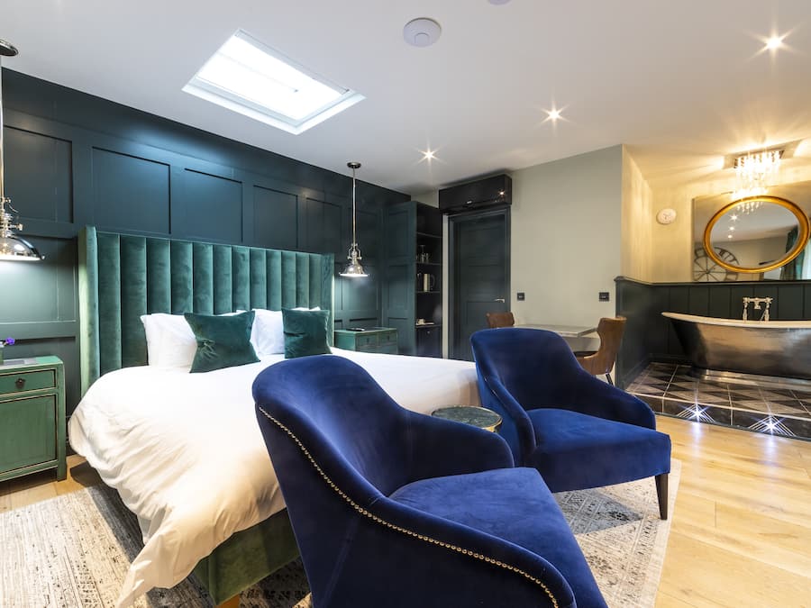 Ein modernes Schlafzimmer mit einem großen Bett, zwei blauen Sesseln, einem Schminktisch mit Spiegel und einer Badewanne.