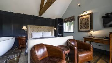 A bedroom with a large bed, two leather chairs, a desk, a television, and a bathtub.