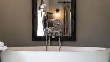 Un baño moderno con una bañera independiente, un espejo grande y un grifo empotrado en la pared.