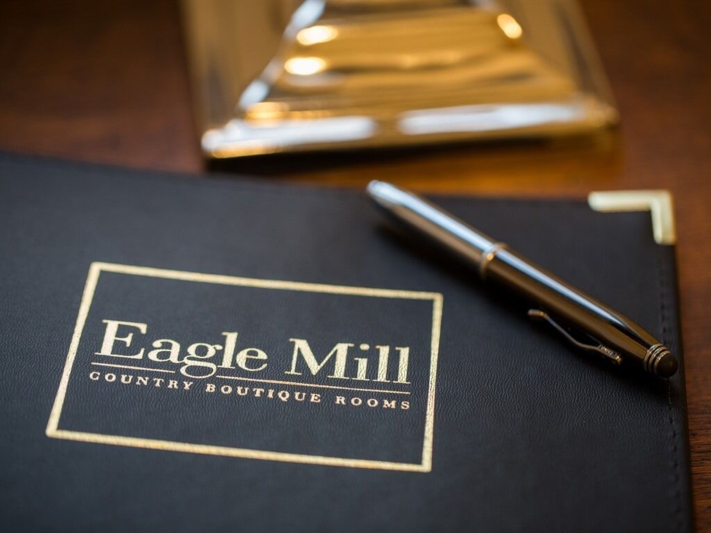 A black folder with "Eagle Mill Country Boutique Rooms" printed on it, a pen, and a blurred background.