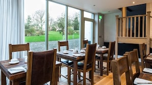 Un comedor con mesas y sillas de madera, ventanas amplias con vistas a un paisaje verde.