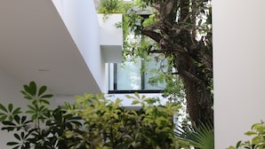 Un edificio moderno con balcón de cristal, rodeado de abundante vegetación.
