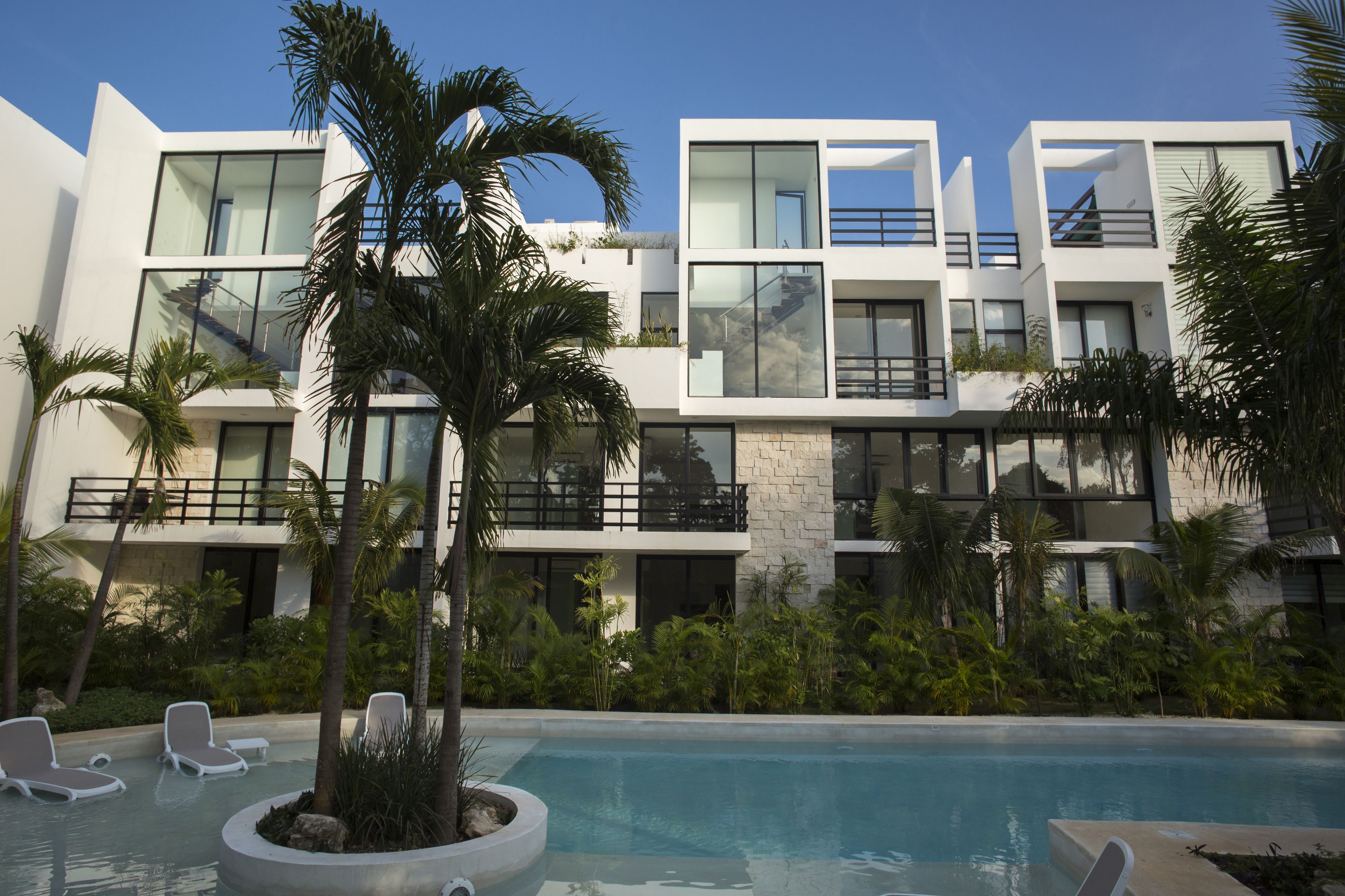 A modern hotel with a pool, palm trees, and a clear blue sky.