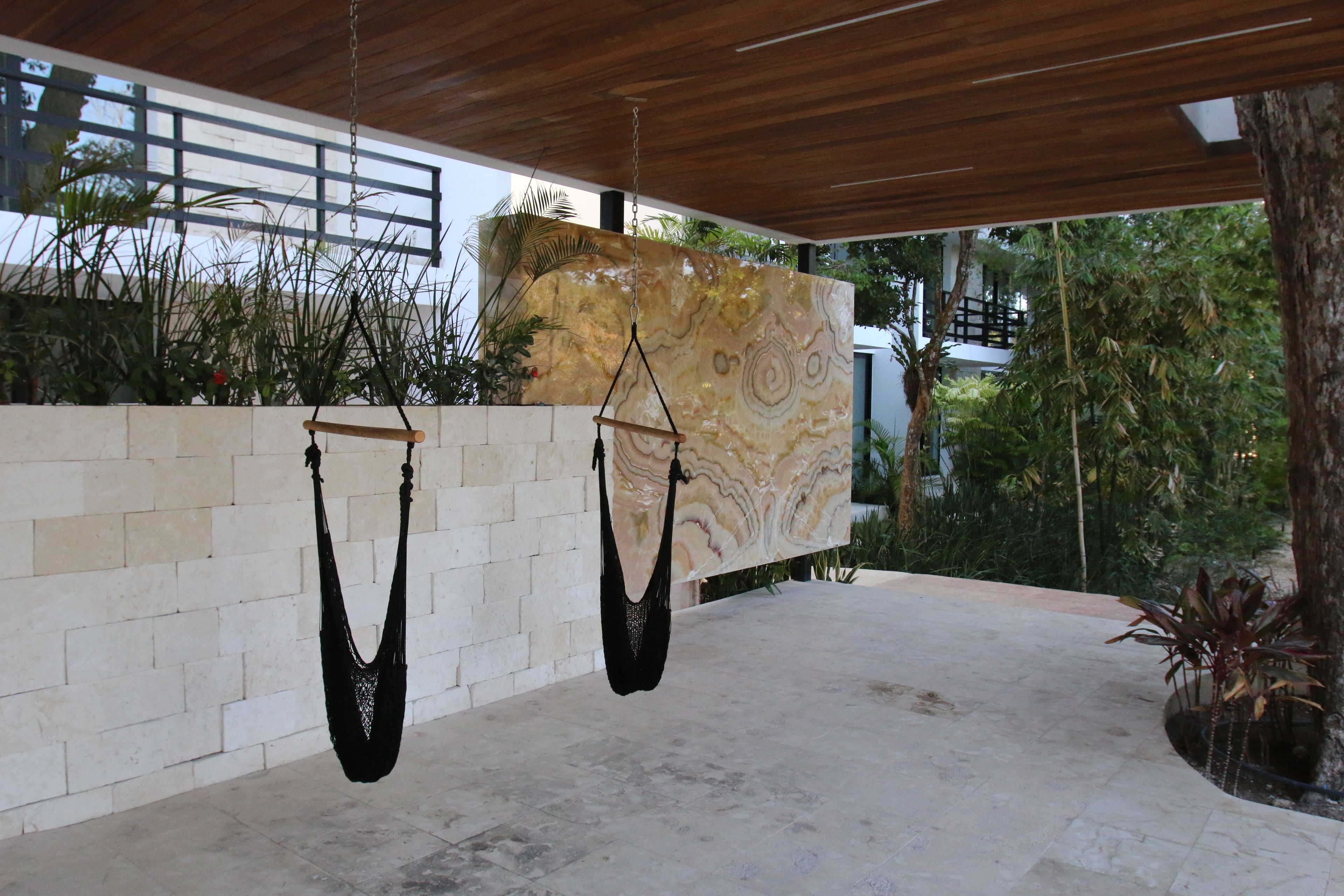 A modern outdoor space with hanging hammocks, a stone wall, and lush greenery.