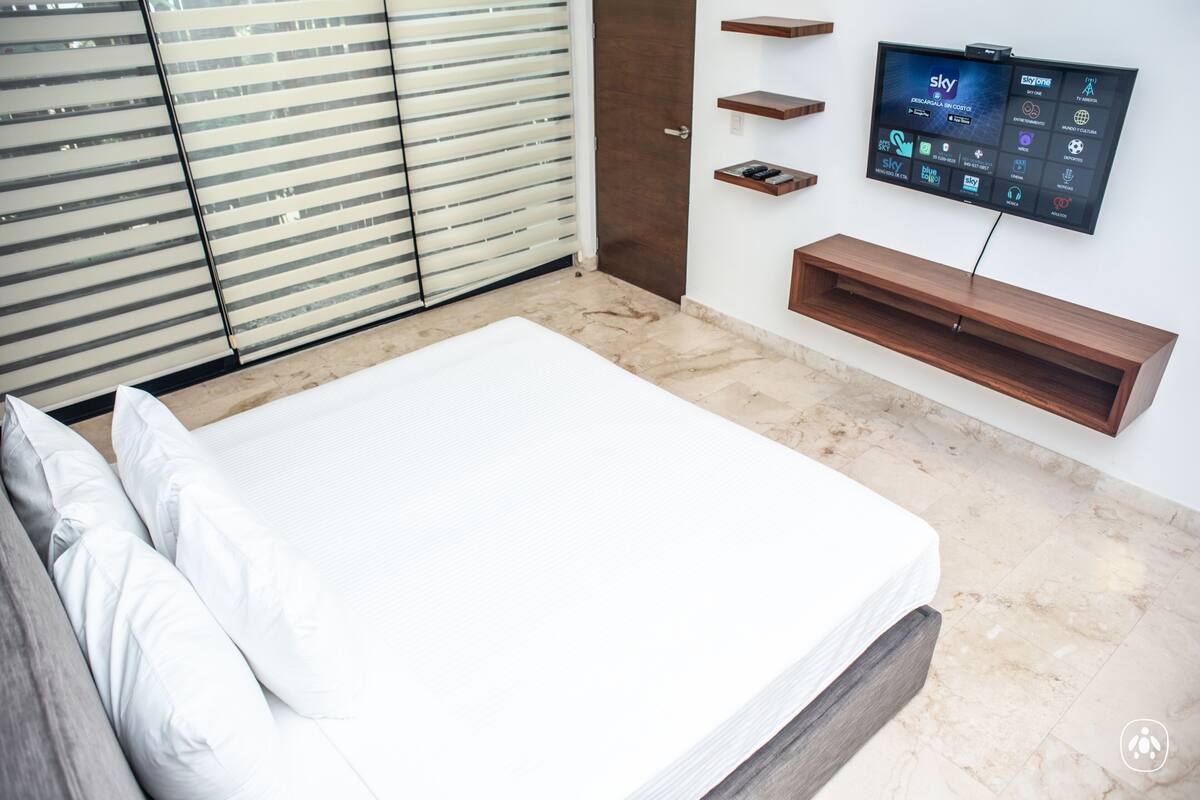 A modern bedroom with a bed, a TV mounted on the wall, and a sliding door.