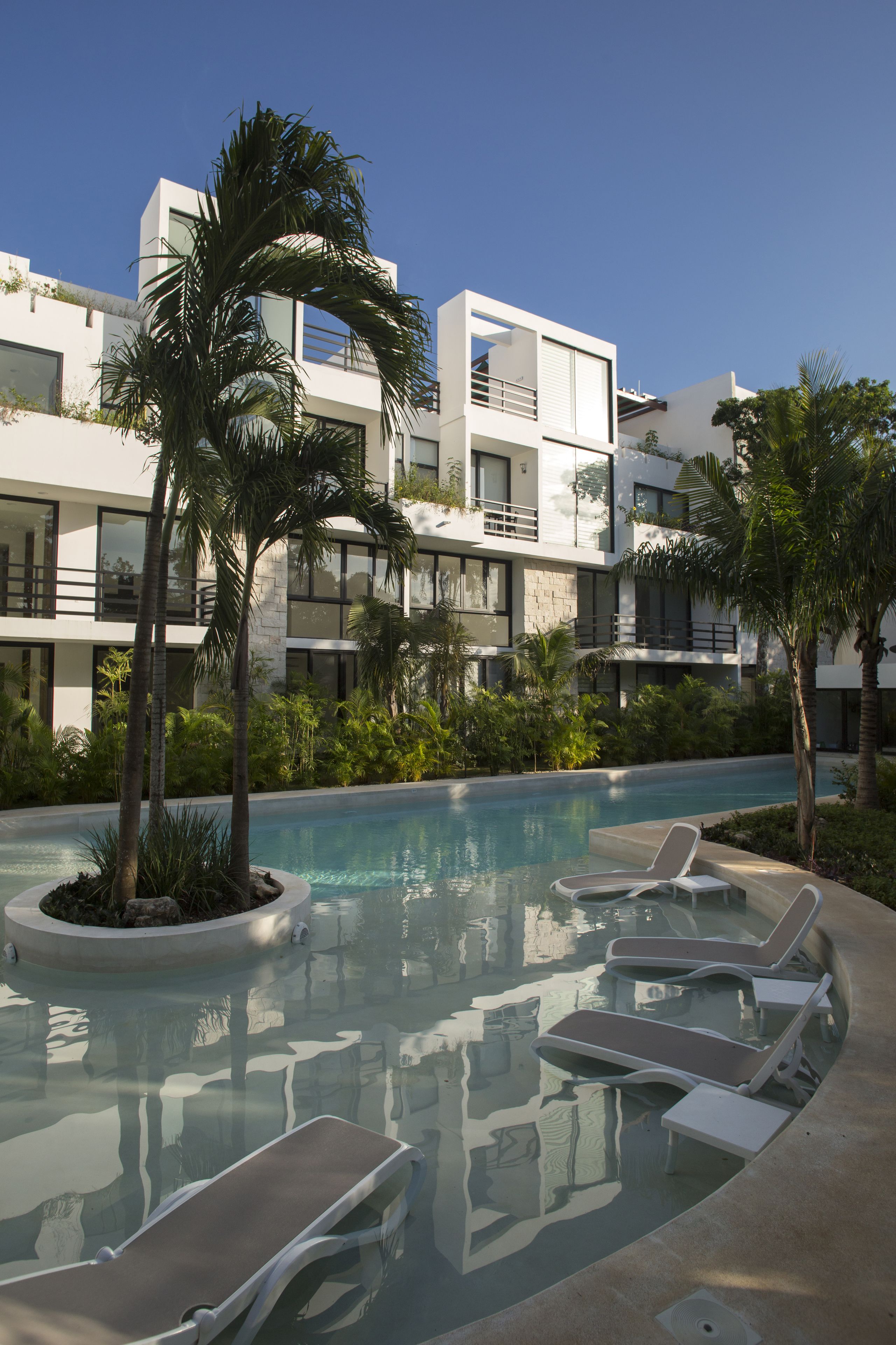 Um hotel moderno com piscina, cadeiras de descanso e palmeiras.