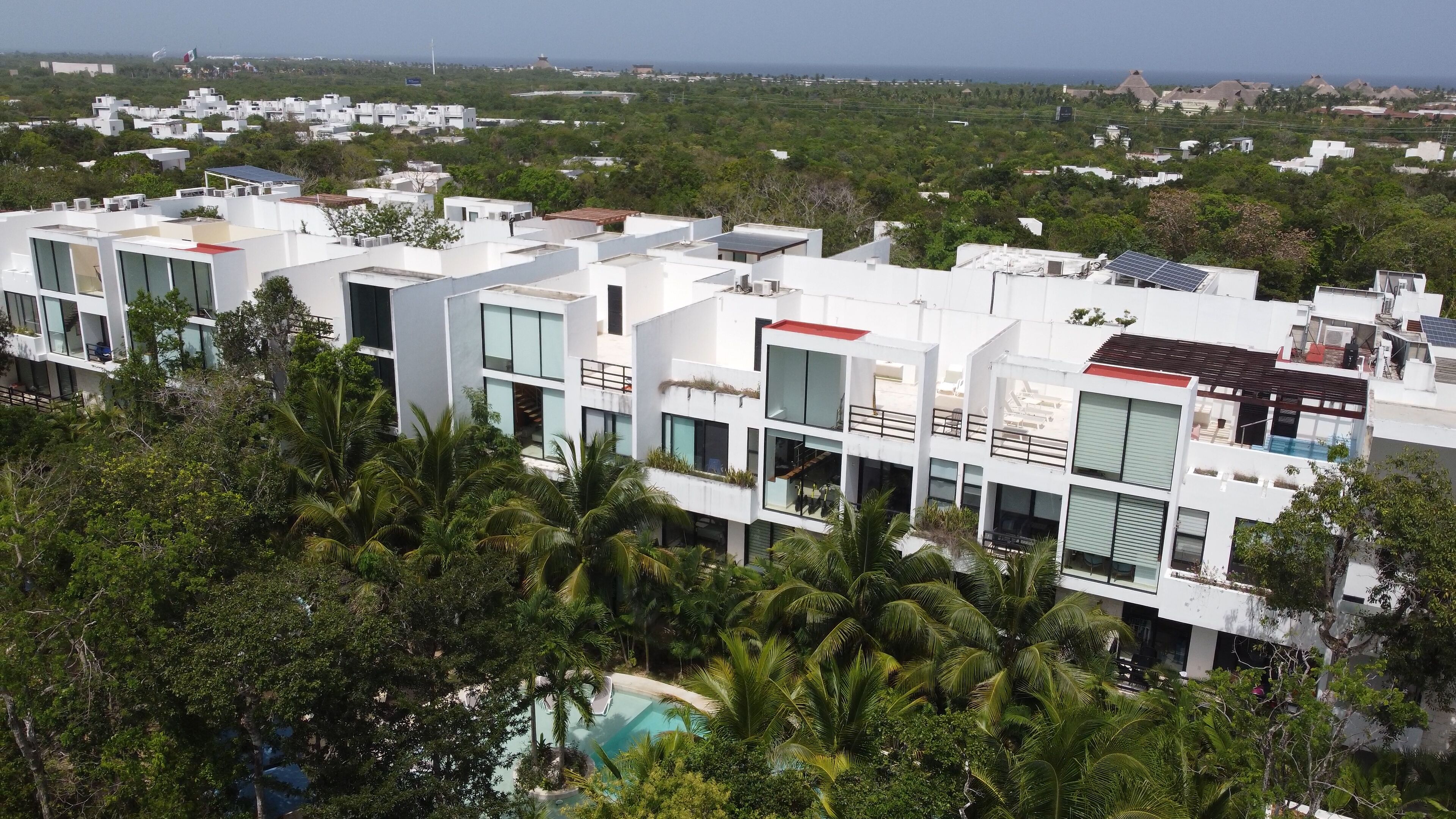 Un moderno complejo residencial con varias edificaciones blancas, paneles solares y una piscina rodeada de exuberante vegetación.