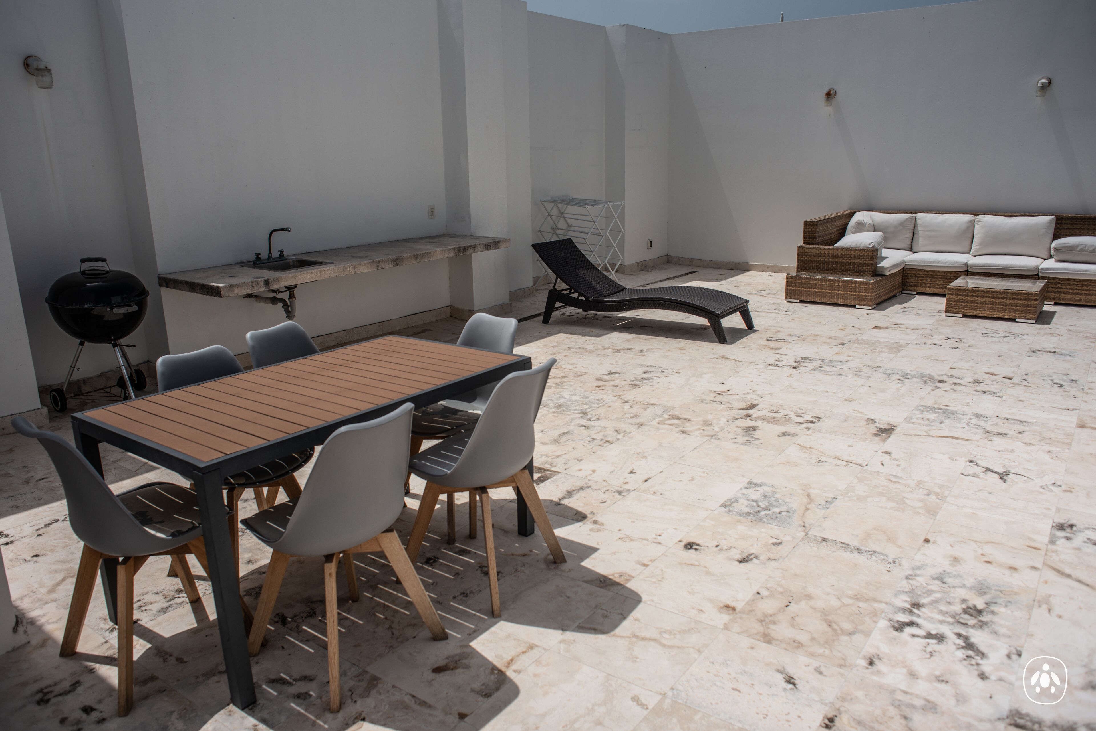 An outdoor patio with a wooden table and chairs, a grill, a sofa, and a small seating area.