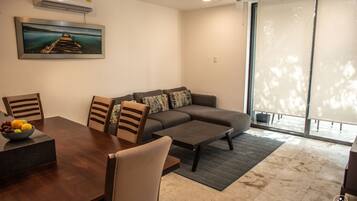 A modern living room with a dining table, sofa, and chairs. There is a painting on the wall and a ceiling fan.