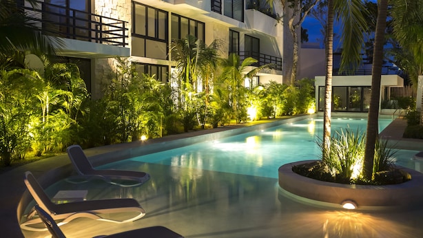 Un hotel moderno con piscina, sillas de descanso y abundante vegetación.