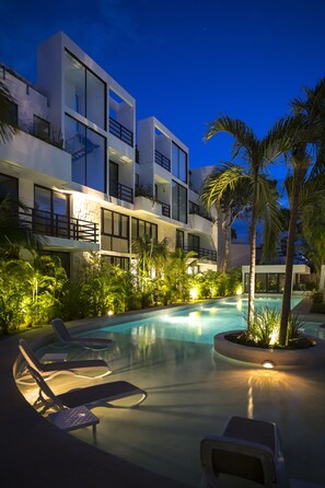 Un hotel moderno con piscina, sillas de descanso y abundante vegetación.