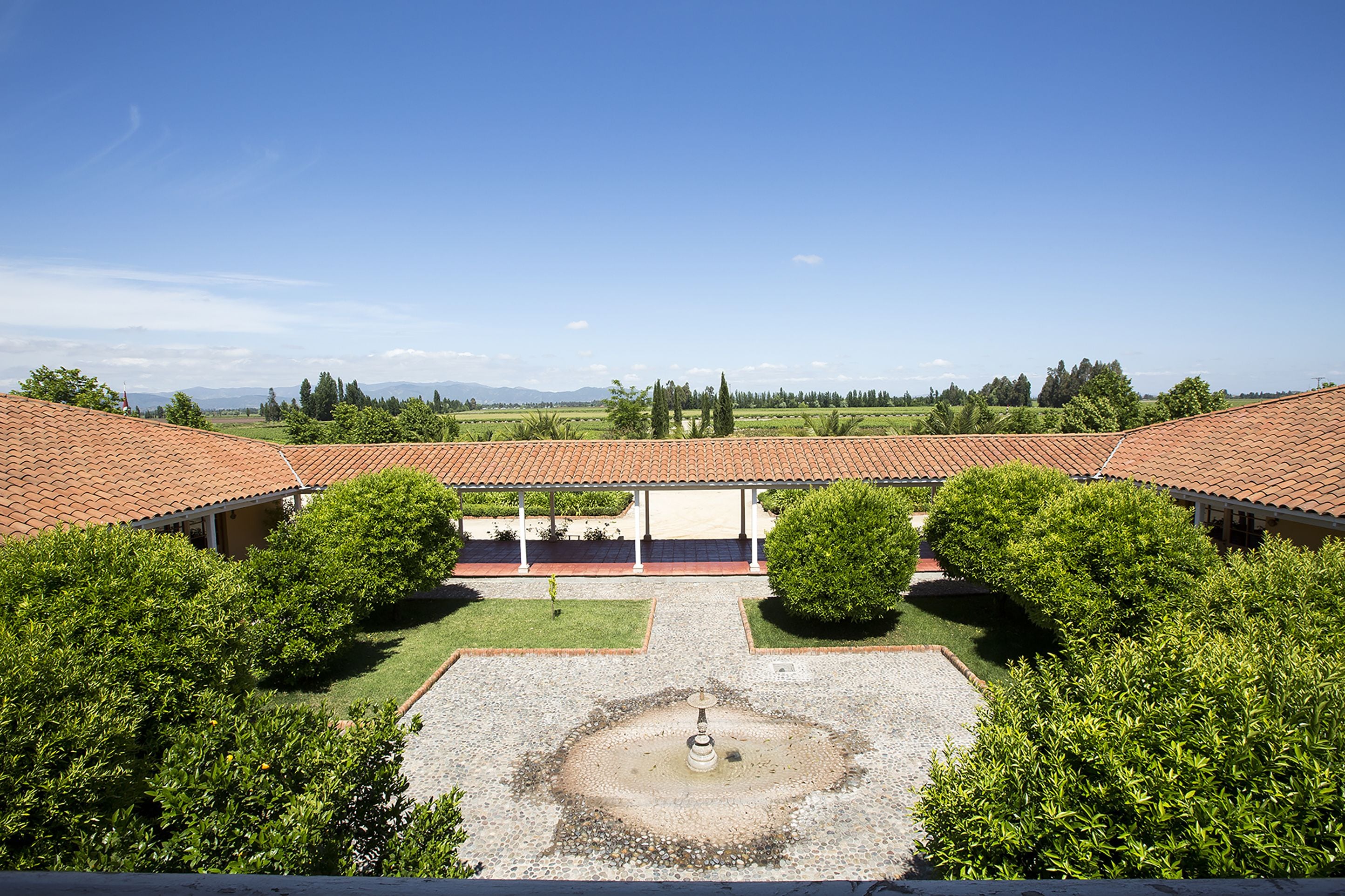 A courtyard with a central fountain, surrounded by trees and buildings with red-tiled roofs.