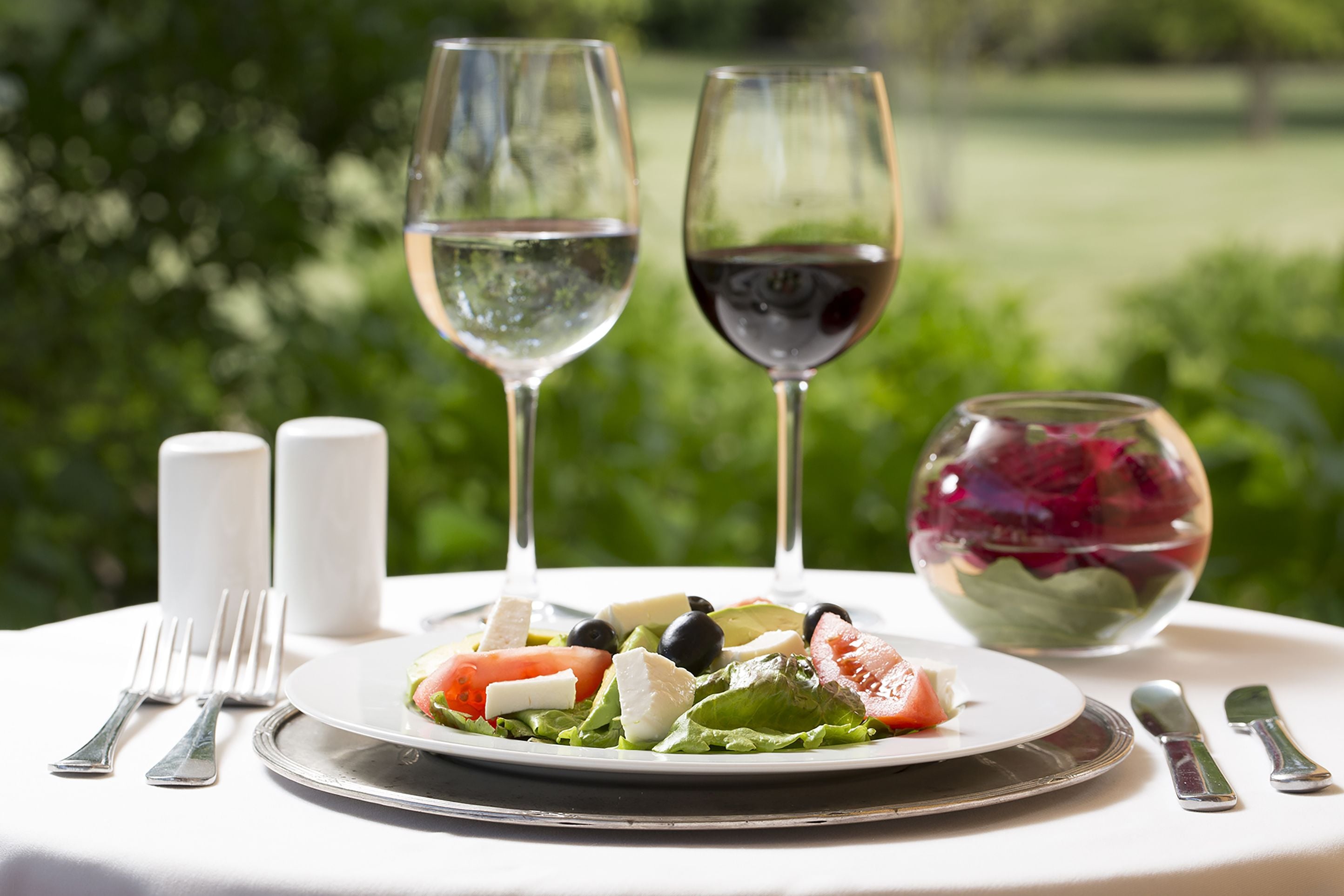 A table set with a plate of salad, two wine glasses, salt and pepper shakers, and cutlery.