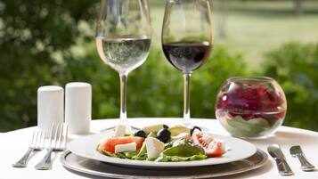 A table set with a plate of salad, two wine glasses, salt and pepper shakers, and cutlery.