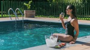 Eine Person entspannt am Pool mit einem Getränk, einem Glas Wasser und einer Snackplatte.