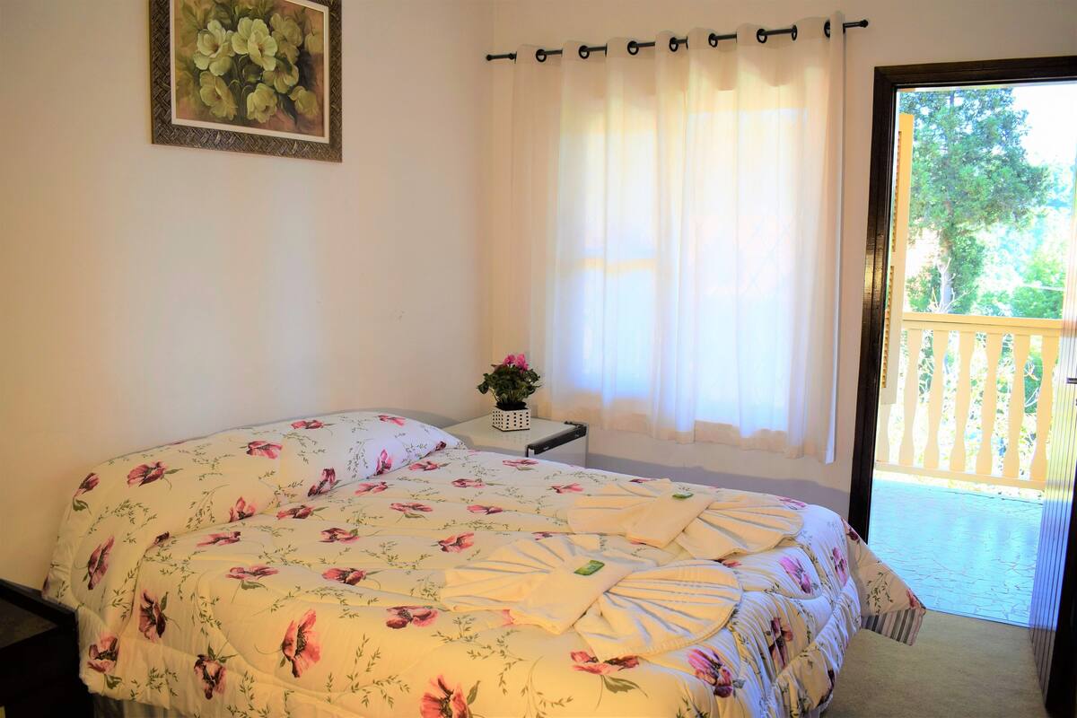 Ein Schlafzimmer mit floralem Bettüberwurf, einem Nachttisch mit Pflanze und Blick auf einen Balkon.