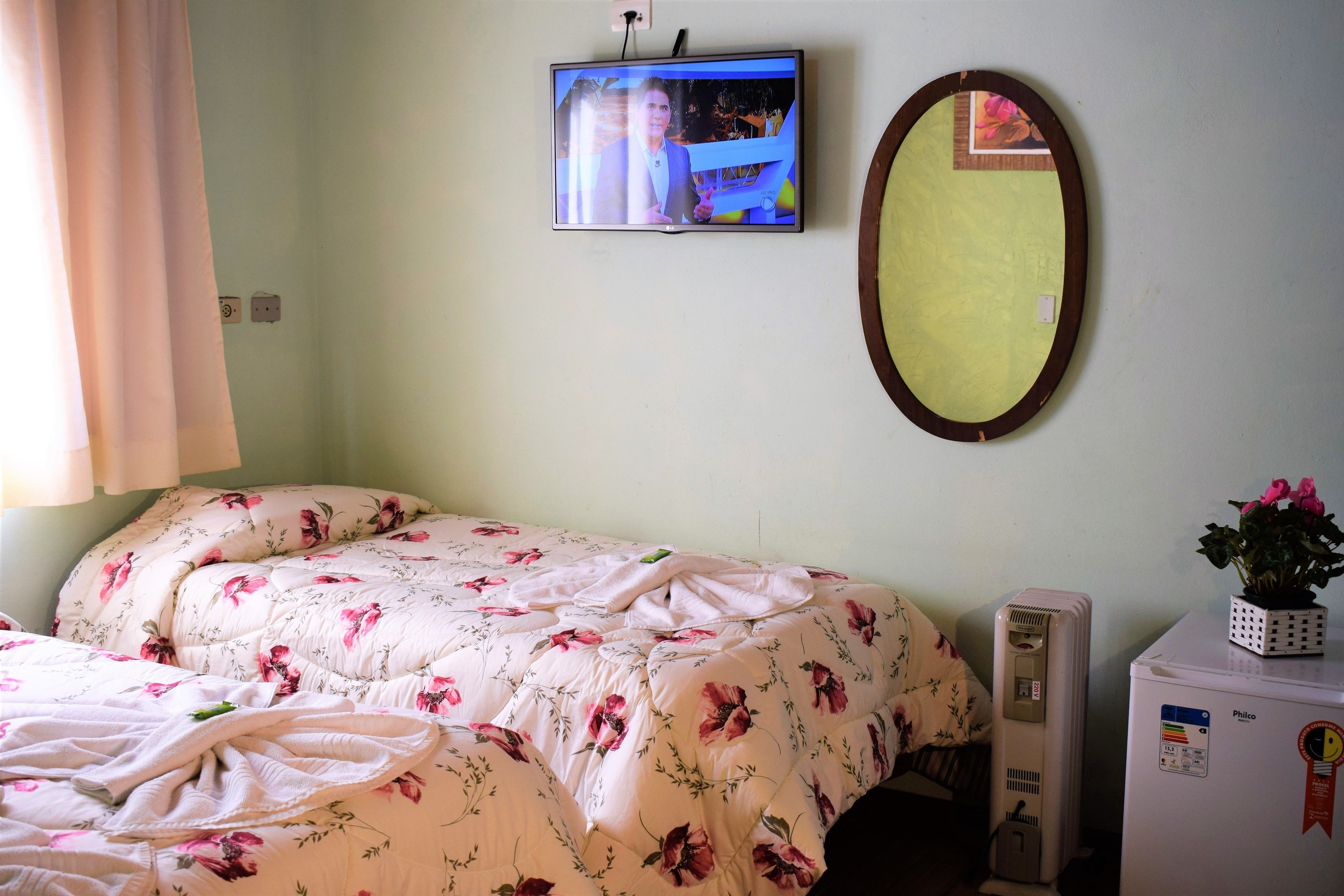 Ein Schlafzimmer mit einem Bett, einem an der Wand montierten Fernseher, einem Spiegel und einem kleinen Kühlschrank.