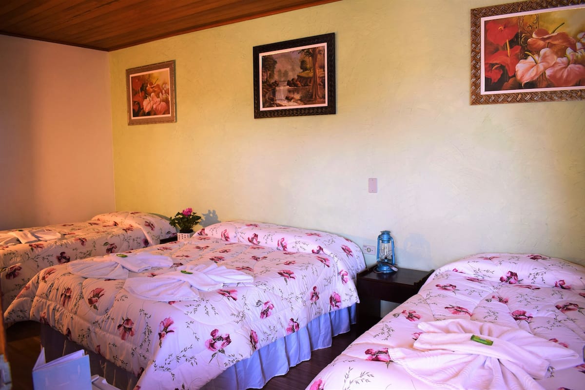 Ein Zimmer mit zwei Betten, jeweils mit Blumenbettwäsche und einem blauen Nachttisch. An der Wand hängen gerahmte Bilder.