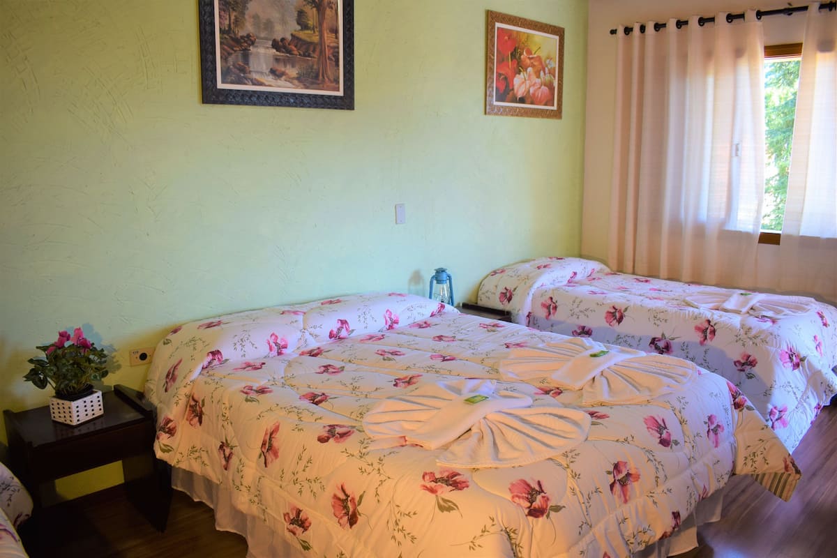 Ein Schlafzimmer mit zwei Betten, floraler Bettwäsche, einem kleinen Tisch mit einer Pflanze und zwei gerahmten Bildern an der Wand.
