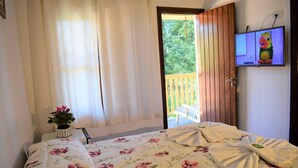 Un dormitorio con cama, televisor, ventana con cortinas y vistas al exterior.