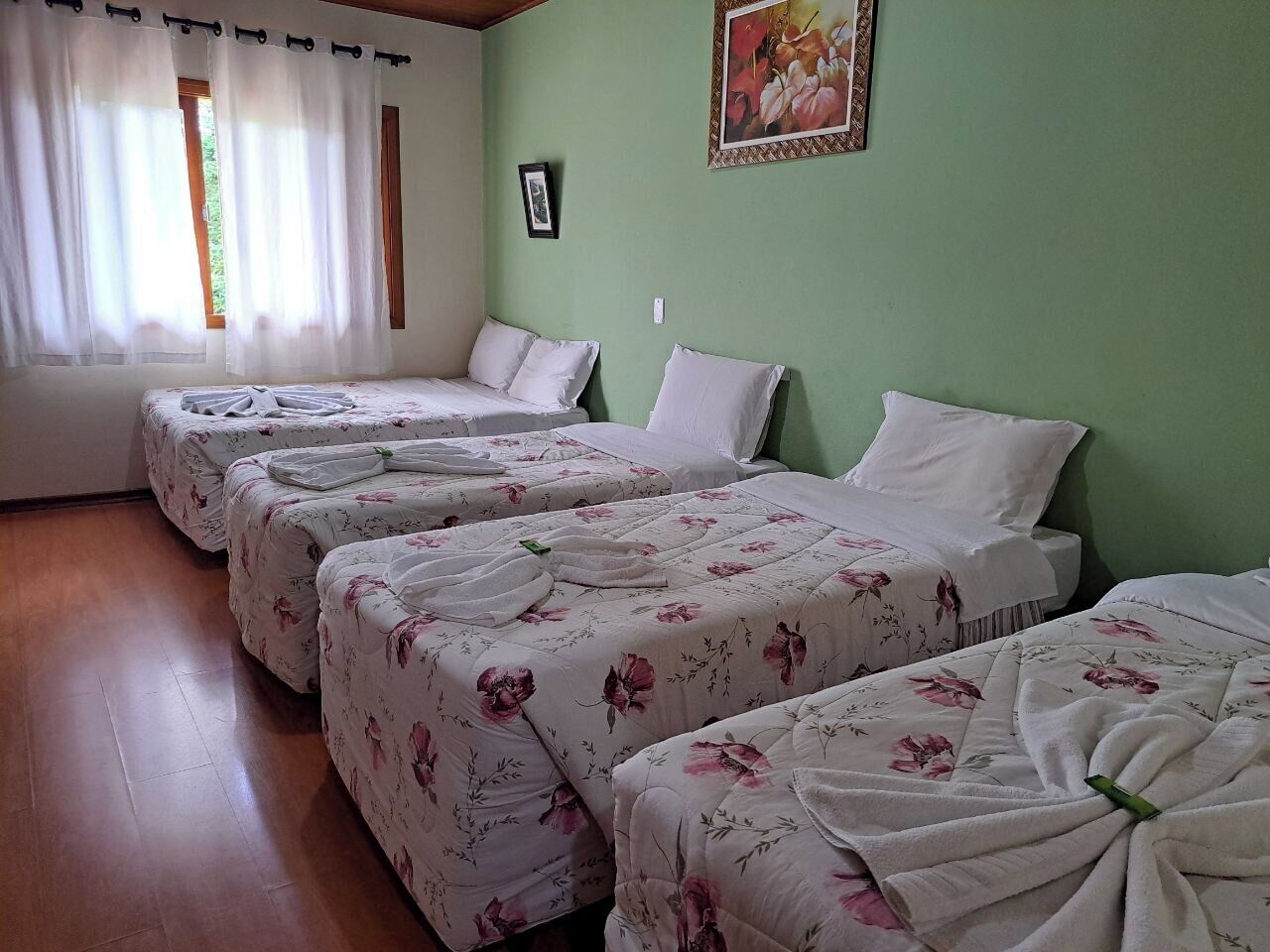 A hotel room with four beds, each with floral bedding and towels neatly arranged.