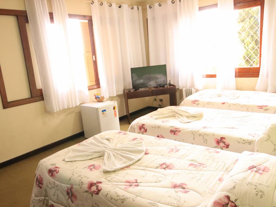 A hotel room with two beds, a television, a small refrigerator, and a window with curtains.