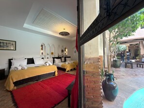 Een hotelkamer met twee bedden, een roodgekleurd tapijt, een grote vaas en uitzicht op de binnentuin.