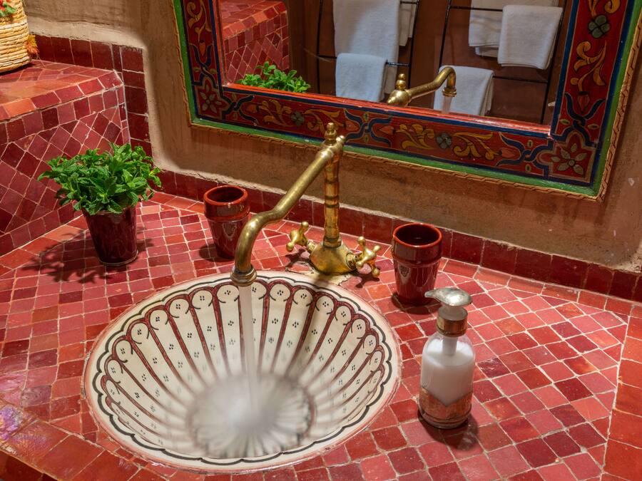 Un baño con un lavabo de azulejos rojos, un grifo de latón y un espejo con marco decorativo.