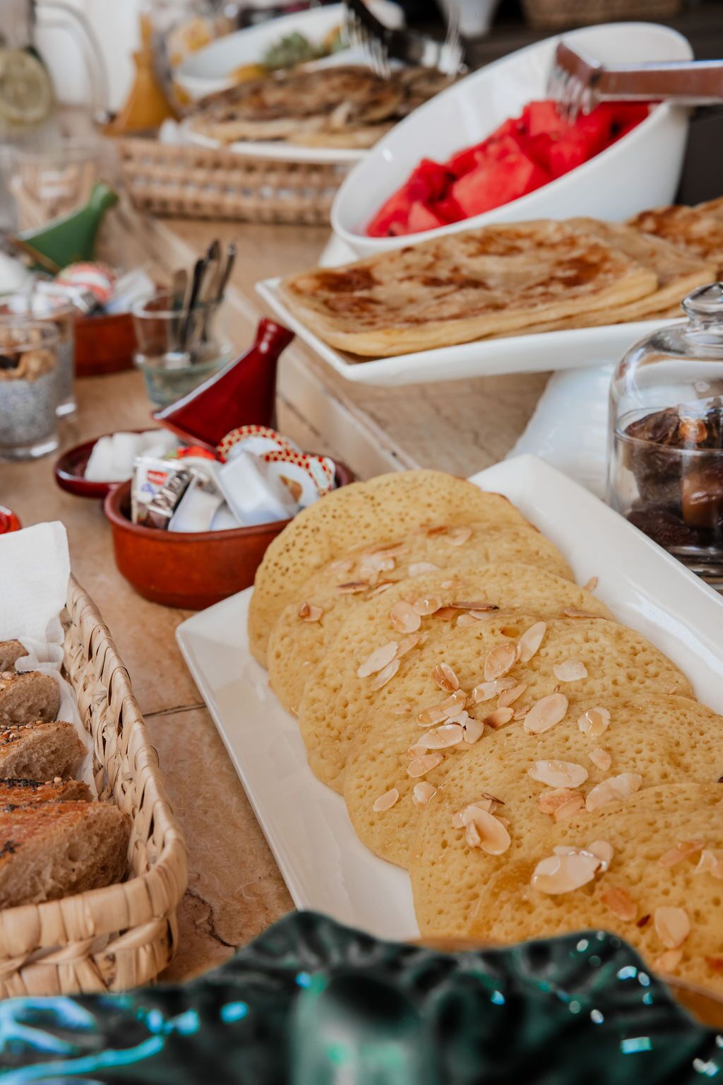 Una mesa con diferentes alimentos, incluyendo pan, un bol de tomates en rodajas y un tarro de vidrio.