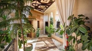 An indoor corridor with a patterned rug, potted plants, and a geometric ceiling design. - Les Sources Berbères Riad & Spa (Marrakech)