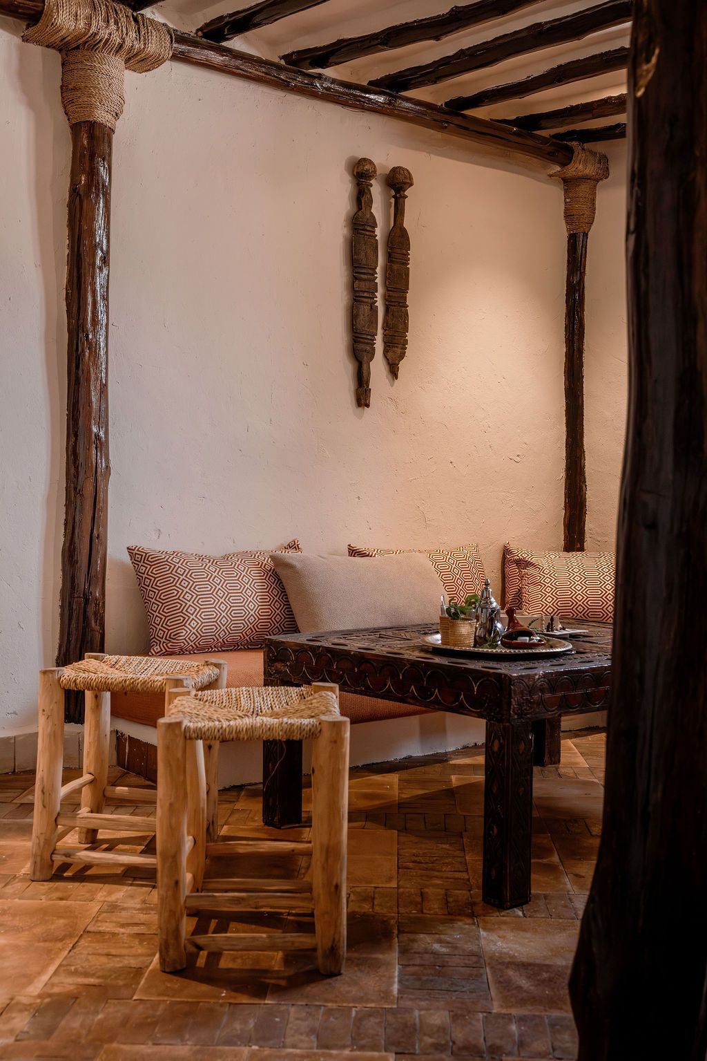 A rustic interior with a wooden bench, woven stools, and a patterned sofa.