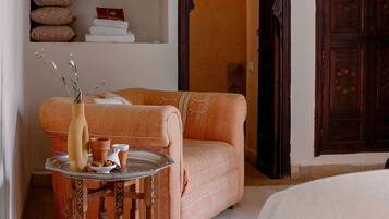 A room with a sofa, a small table with a vase and a pitcher, and a shelf with patterned pillows and a book.